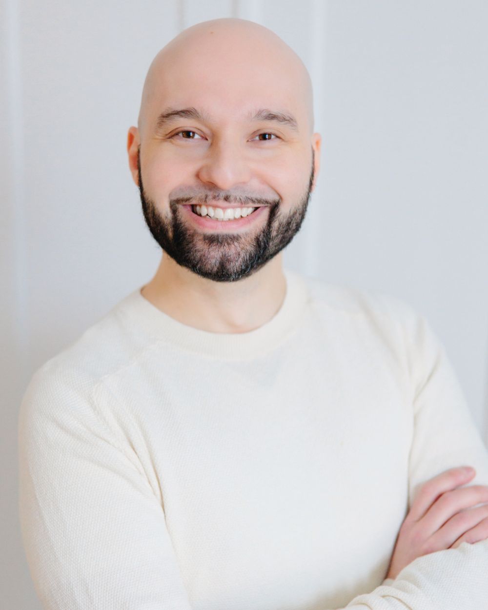 Niko Karppinen smiling with arms folded, wearing a cream knit jumper against a pale wall